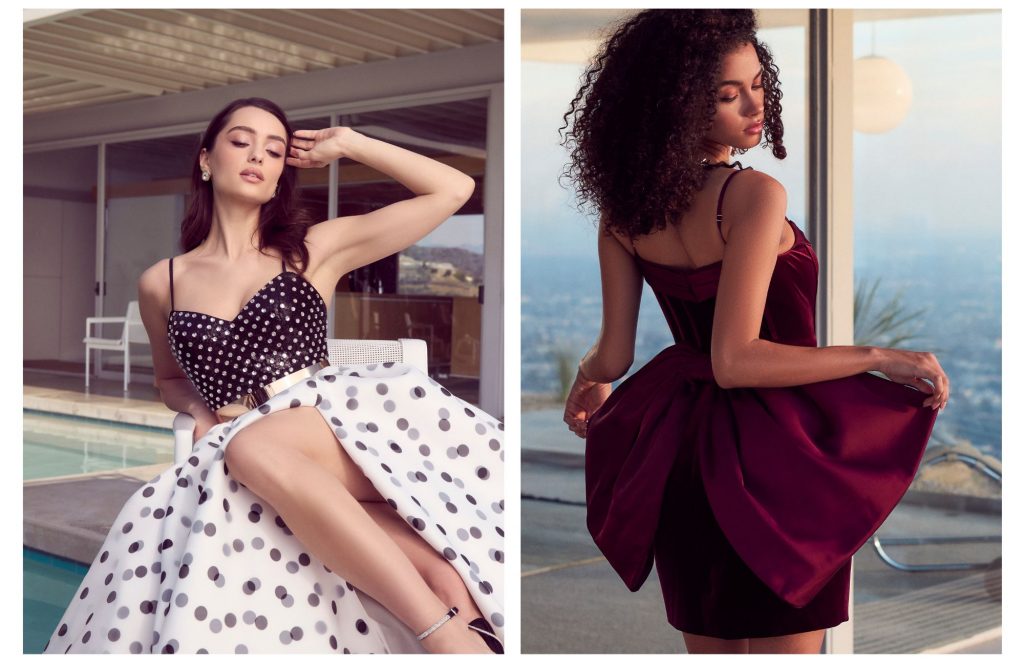 A women sitting down on a patio wearing the Gwen Black and White Polka Dot Contrast Gown and a woman in in Joanna Wine Bow Mini Dress posing in front of a window.